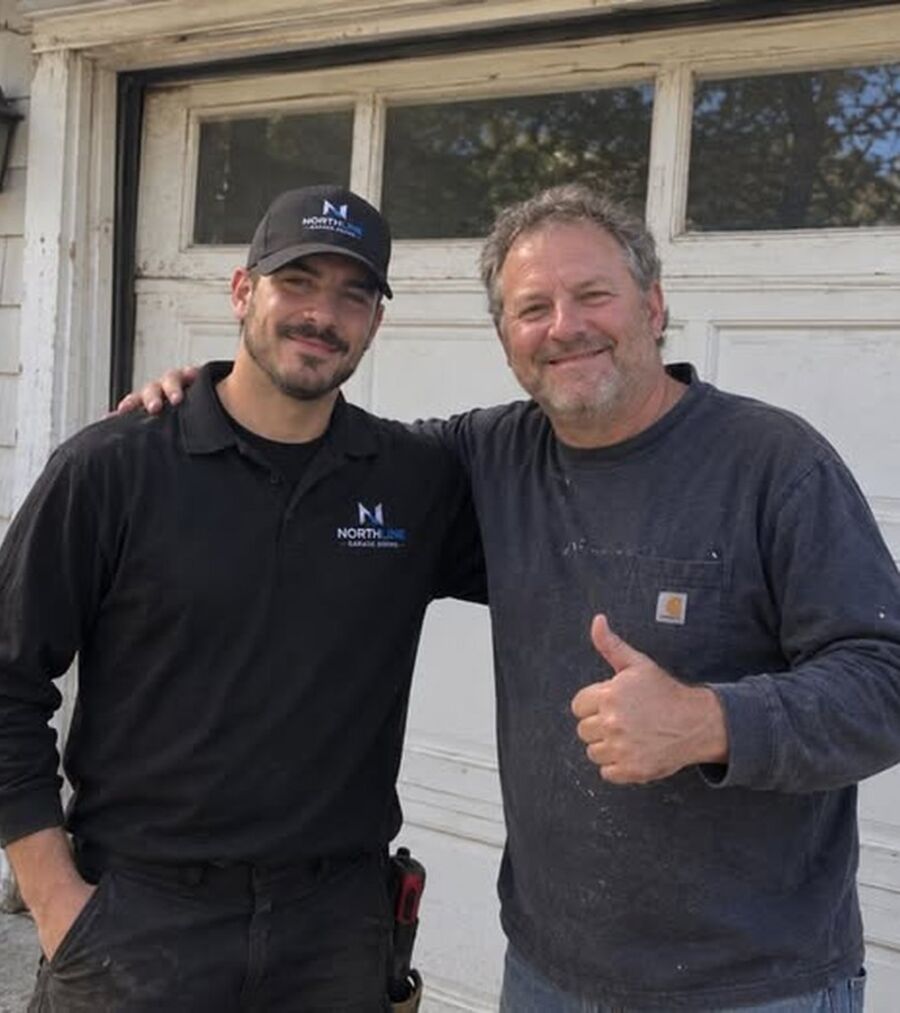 Two men smiling in front of a garage, one wearing a NorthLine shirt