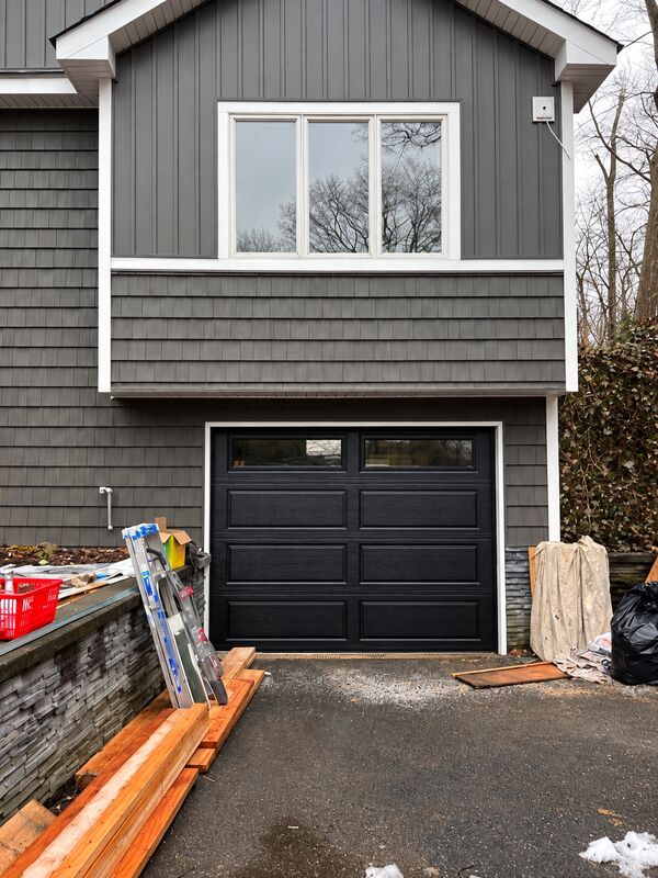 Black garage door with a row of windows across the top, set in gray shingle siding